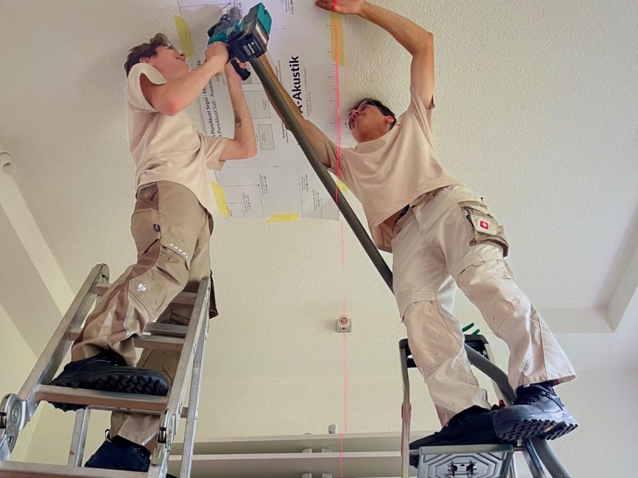 Zwei Handwerker auf Leitern, die eine Deckenmontage mit einem Laser ausrichten.